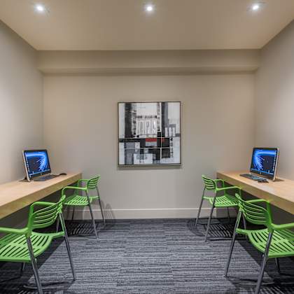 a room with green chairs and laptops on wooden desks.