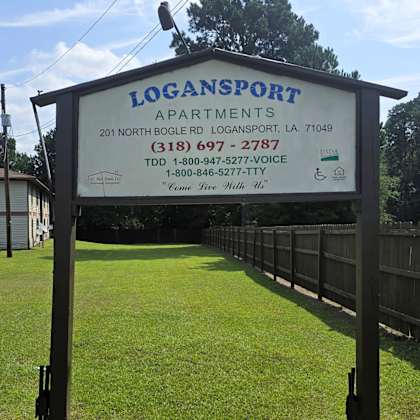 a sign for logansport apartments is displayed in front of a grassy area.