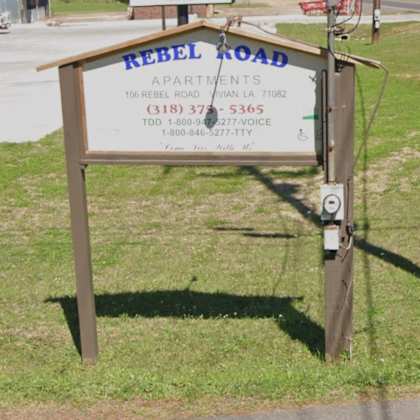 a sign for rebel road apartments is displayed in front of a grassy area.