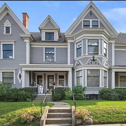 a large, grey victorian-style house with a front porch and a staircase leading to the entrance.