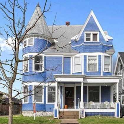 a blue house with a white fence and a tree in front.