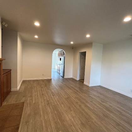 a spacious room with wooden flooring and a fireplace on the left side.