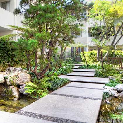 a garden with a stone pathway leading to a pond at sunset barrington gardens, los angeles, 90049