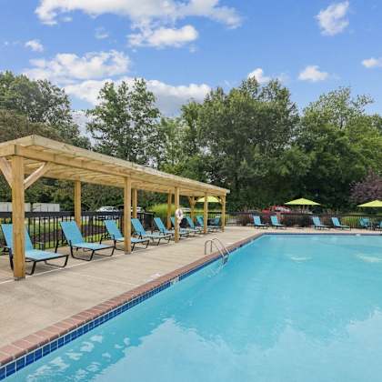 a swimming pool with blue chairs and a wooden pavilion next to it at the grove at lyndon, louisville