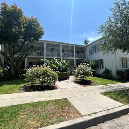 a sunny day at a white building with trees and bushes in front.