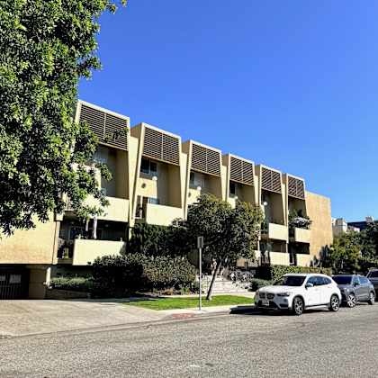 a white car is parked in front of a building with a tree to the left.