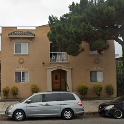 a silver minivan is parked in front of a tan house with a black car parked behind it.