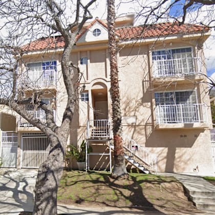 a beige two-story building with a red tile roof and a balcony on the second floor.