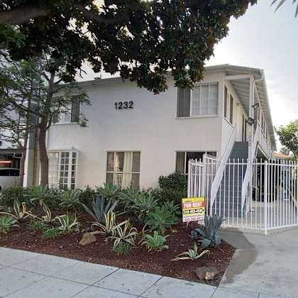 a house with the number 1232 on it is surrounded by a white fence and has a sign in front of it.