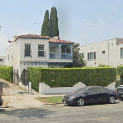 a black car is parked in front of a white house with a red tile roof.