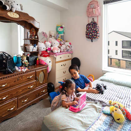 two children playing with toys in a room with a wooden dresser and a window.