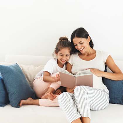two people are sitting on a couch, one is reading a book to the other.