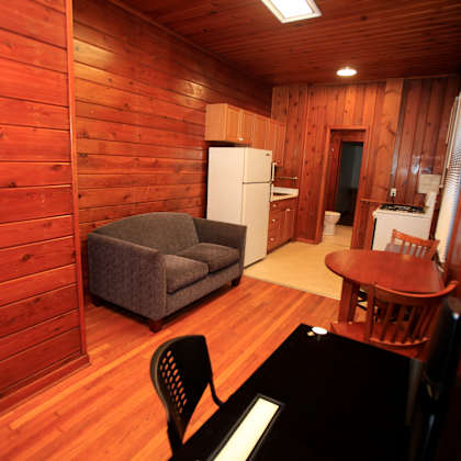 a small room with a couch, chair, table and a refrigerator.