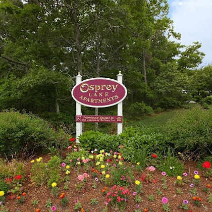 a sign for osprey landings apartments is surrounded by flowers.
