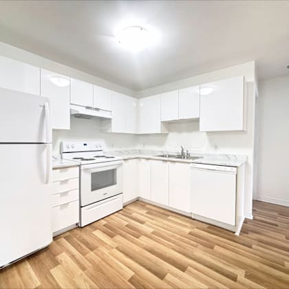 a white kitchen with wooden floors and white appliances.