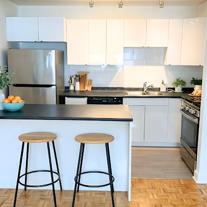 a kitchen with white cabinets and a black countertop with a refrigerator, stove, and two bar stools.