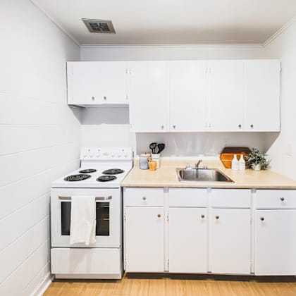 a white kitchen with a stove, sink, and cabinets.