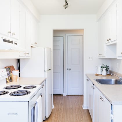 a white kitchen with a stove, sink, and cabinets.