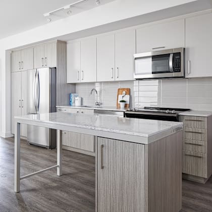 a modern kitchen with a stainless steel refrigerator, microwave, and a marble countertop.