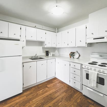 a white kitchen with wood floors and white appliances.