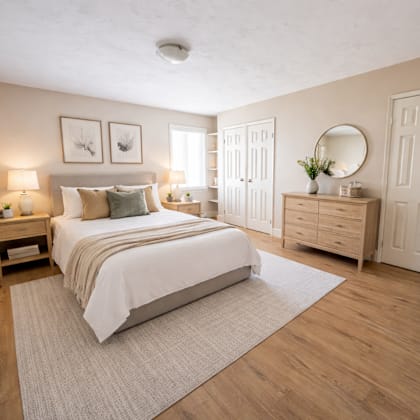 a bedroom with a large bed, a nightstand with a lamp, and a dresser with a mirror.