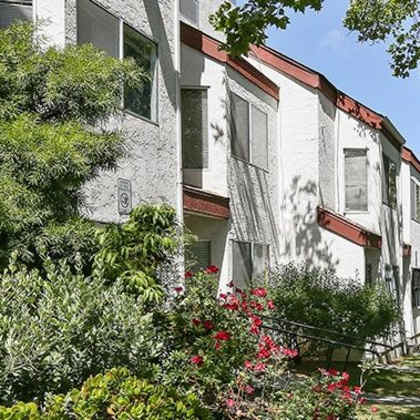 a row of white houses with red trim and green trees in front.