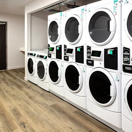 a row of white front load washing machines are lined up in a laundromat.