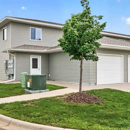 a tree in front of a grey house with a green utility box.