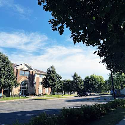 a parking lot in front of a building with trees and a clear sky.