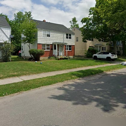 a residential street with houses on both sides and a white car parked on the right side.