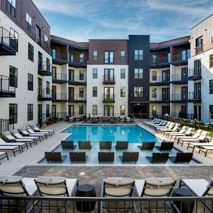 a swimming pool surrounded by lounge chairs in front of apartment buildings.