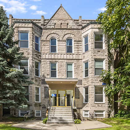 a large, historic-looking building with a front porch and a tree in front.