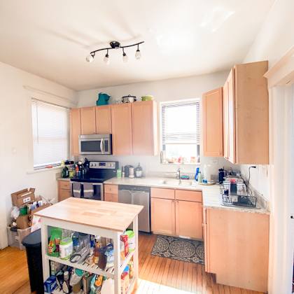 a kitchen with wooden floors and a table with a black trash can underneath it.