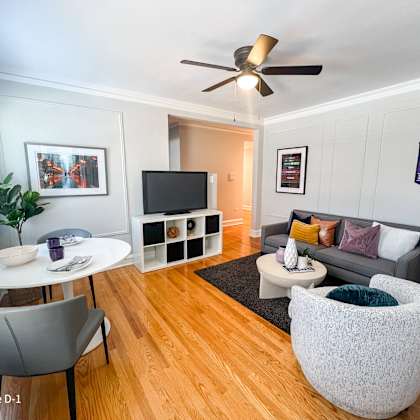 a living room with a white sofa, a white coffee table, a grey chair, a white table and a tv.