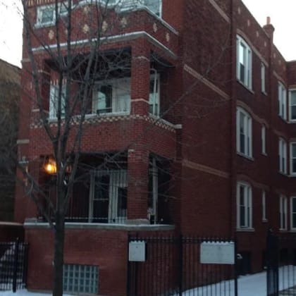 a red brick building with a black fence and a red fire hydrant in front of it.