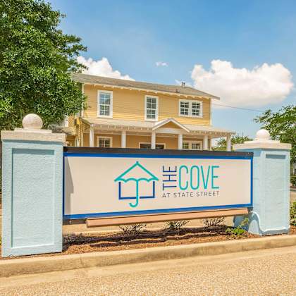 a sign for el cove at state street in front of a yellow house. at the cove at state street apartments, baton rouge, la