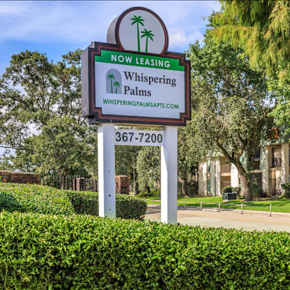 a sign for whispering palms apartments is displayed in front of a building.