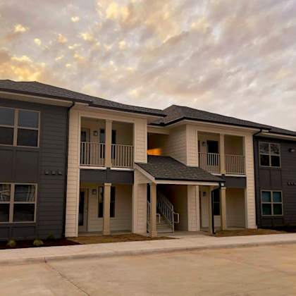 an apartment building with a parking lot and a cloudy sky