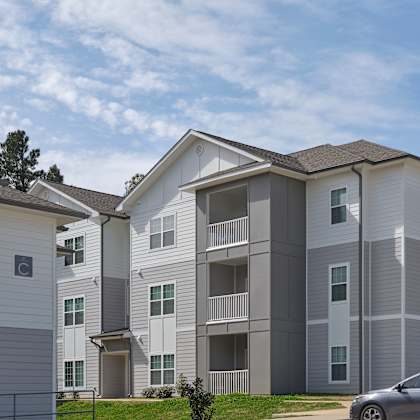 a grey and white apartment building with a car parked in front.