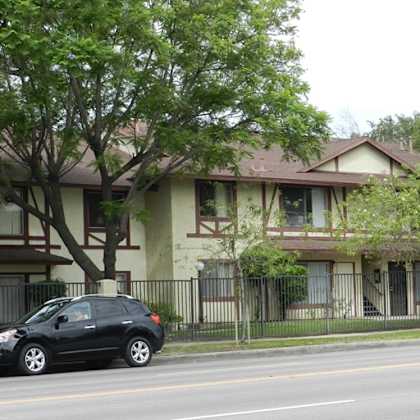 a black car is parked on the side of a street in front of a two-story house.