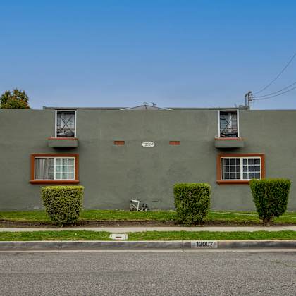 a green house with two windows and a white sign on the street.