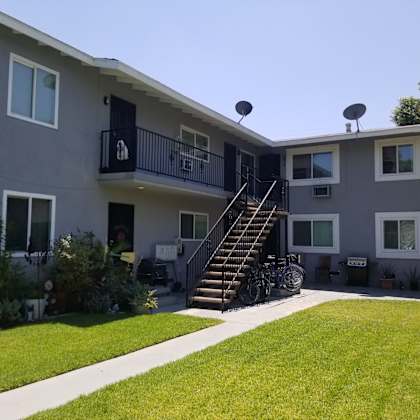 a grey two-story apartment building with a balcony and stairs leading to the second floor.
