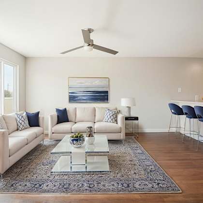 a modern living room with a white sofa set, a glass coffee table, and a ceiling fan.