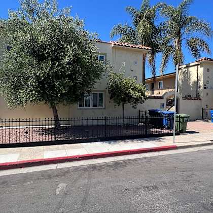 a car is parked under a tree with a building in the background.