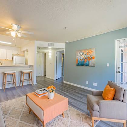 a living room with a grey couch, orange pillows, and a painting on the wall.