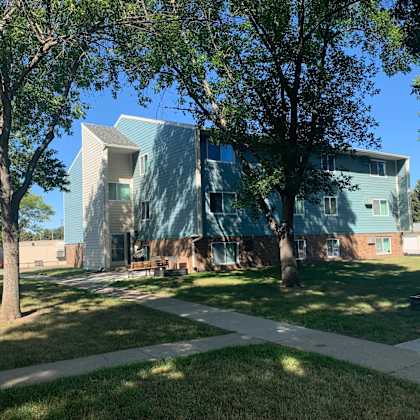 a modern building with a greenish hue is surrounded by trees and grass.