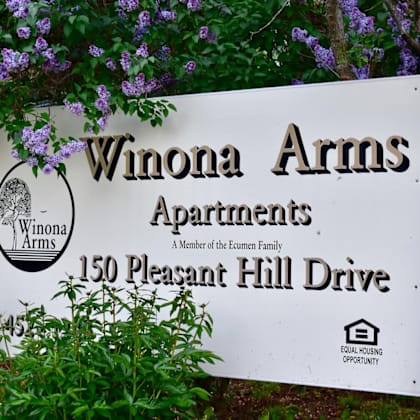 a sign for winona arms apartments is displayed in front of some purple flowers.