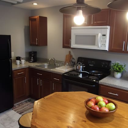 a kitchen with a black refrigerator, wooden cabinets, a black stove, and a wooden table with a bowl of fruit on it.