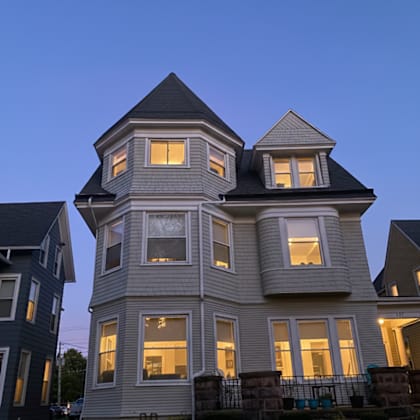 a large house with a tower and multiple windows is lit up at dusk.
