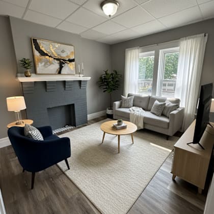 a living room with a blue armchair, a grey couch, a fireplace, and a painting on the wall.